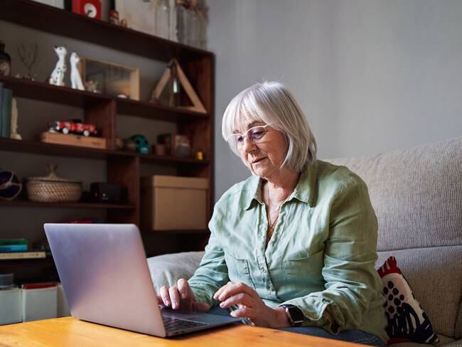 Mujer sentada en el sofá revisando su computadora (Foto vía Getty Images)