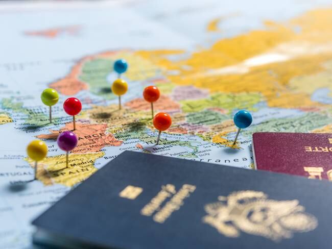 Mapa del mundo con marcaciones en distintos países y un pasaporte azul y rojo (Foto vía Getty Images)