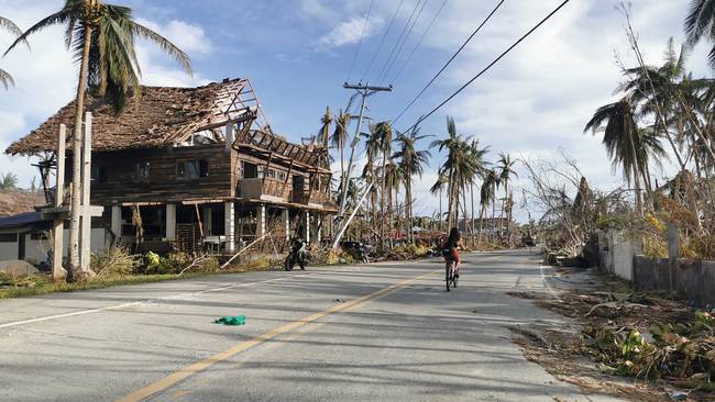 TOPSHOT - A cyclist travels past destroyed vegetation and houses along a road in Dapa town, Siargao island on December 21, 2021, days after super Typhoon Rai devastated the island. (Photo by Ferdinandh CABRERA / AFP) (Photo by FERDINANDH CABRERA/AFP via Getty Images)