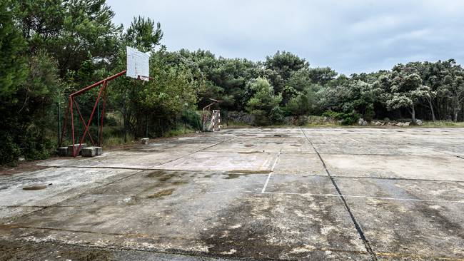 Old abandoned school sports court or schoolyard for different activities. Ruins of a sport venue abandoned long time ago with soccer, handball or football goals, basketball hoops and boards and destroyed concrete plates.