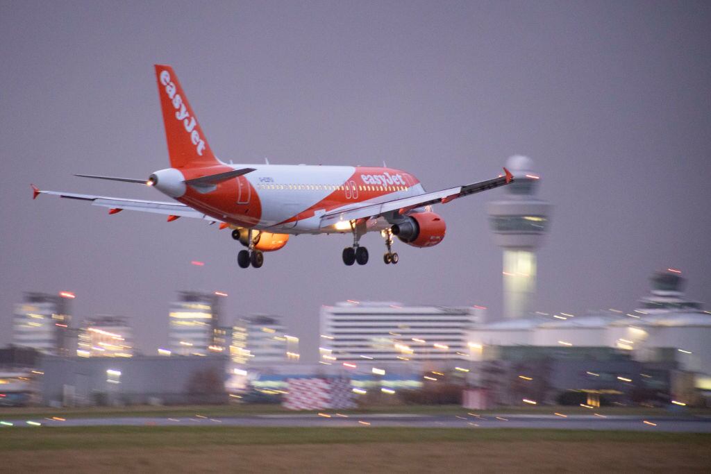 EasyJet Airbus A319 aircraft as seen on final approach flying and landing at Amsterdam Schiphol Airport AMS EHAM with the control tower and the airport terminal in the background in the evening. The arriving airplane of the British multinational low-cost airline has the registration G-EZFU. The aviation industry and passenger traffic is phasing a difficult period with the Covid-19 coronavirus pandemic having a negative impact on the travel business industry with fears of the worsening situation due to the new Omega variant mutation. Amsterdam, the Netherlands on January 5, 2022 (Photo by Nicolas Economou/NurPhoto via Getty Images)
