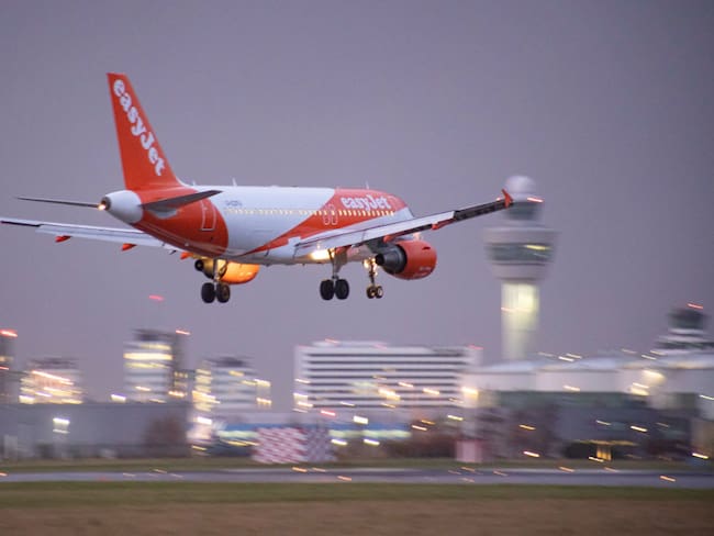 EasyJet Airbus A319 aircraft as seen on final approach flying and landing at Amsterdam Schiphol Airport AMS EHAM with the control tower and the airport terminal in the background in the evening. The arriving airplane of the British multinational low-cost airline has the registration G-EZFU. The aviation industry and passenger traffic is phasing a difficult period with the Covid-19 coronavirus pandemic having a negative impact on the travel business industry with fears of the worsening situation due to the new Omega variant mutation. Amsterdam, the Netherlands on January 5, 2022 (Photo by Nicolas Economou/NurPhoto via Getty Images)