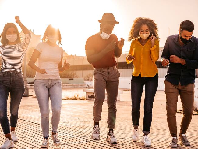 Group of young men and women, friends, wearing protective face masks and dancing at sunset.