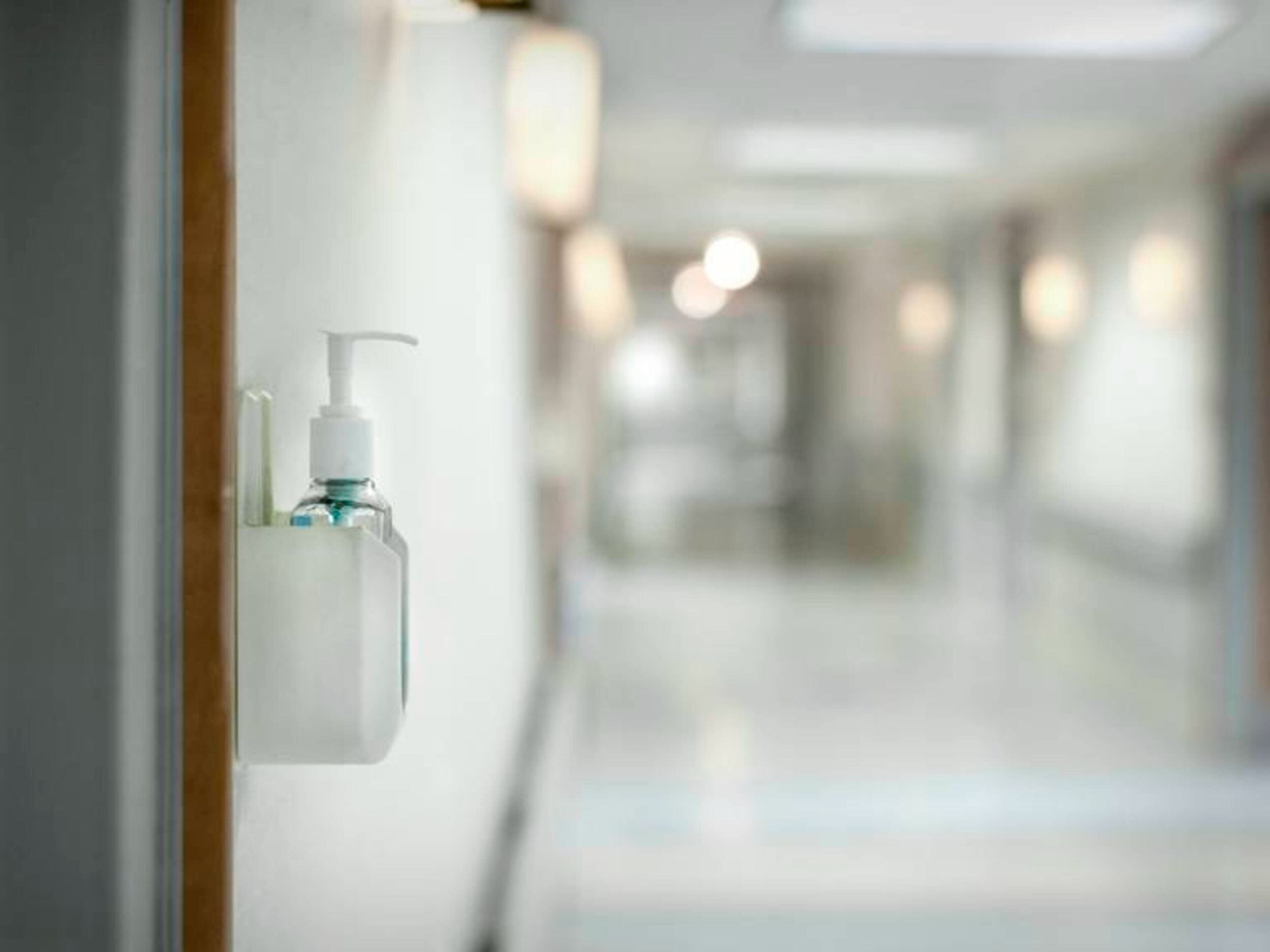 Hand sanitizer dispenser on wall of hospital in hallway / David Sacks