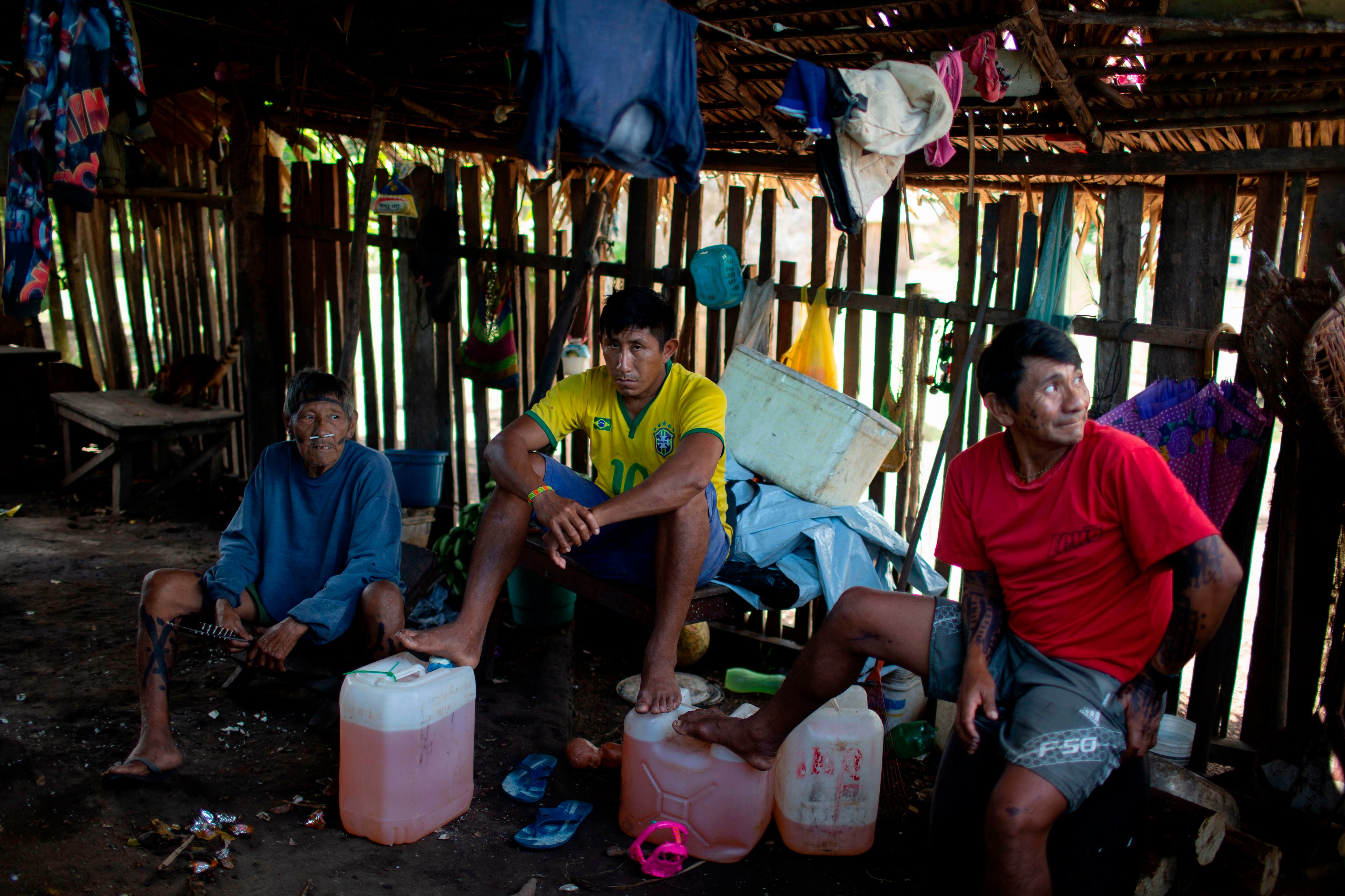 Arara indigenous men sit next jerry cans with petrol at the Laranjal tribal camp, in Arara indigenous land, Para state, in the northern Brazilian Amazon rainforest, on March 15, 2019. - Isolated and off the grid, the nearly 200 residents of Laranjal village on the edge of the Iriri River in Brazil's northern state of Para are among the some 800,000 indigenous people President Jair Bolsonaro says he wants to "integrate into society."Bolsonaro's remarks alarmed the Arara, who like other indigenous groups across Latin America's biggest country have long battled to protect their traditional way of life, away from towns and cities. (Photo by Mauro Pimentel / AFP) (Photo credit should read MAURO PIMENTEL/AFP via Getty Images)