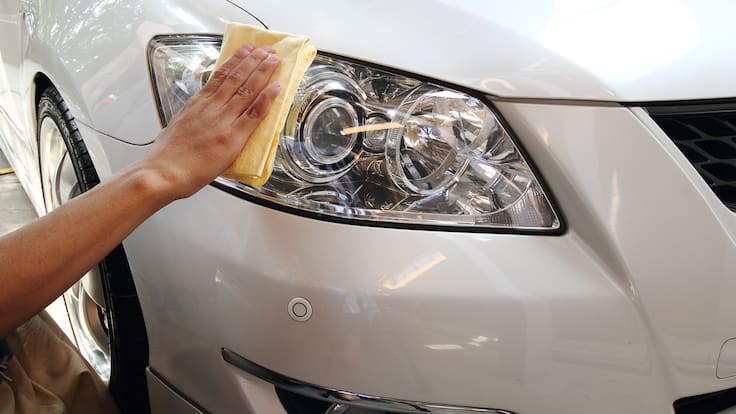 Persona limpiando las luces de un carro blanco con un paño. (Foto vía Getty Images)