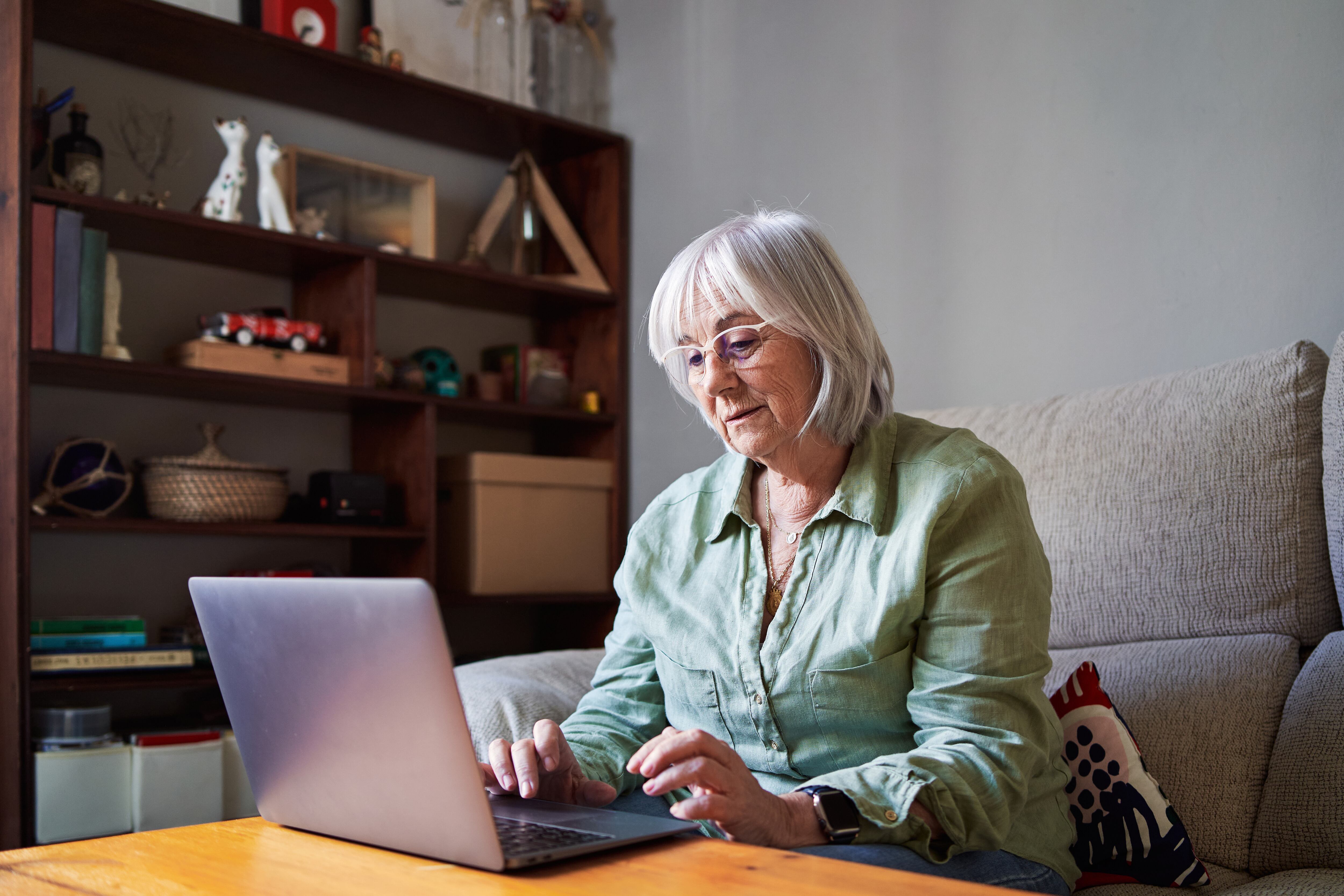 Mujer sentada en el sofá revisando su computadora (Foto vía Getty Images)