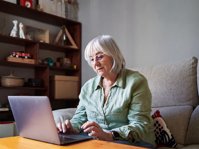 Mujer sentada en el sofá revisando su computadora (Foto vía Getty Images)