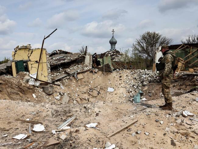 A Ukranian serviceman looks into a crater and a destroyed home are pictured in the village of Yatskivka, eastern Ukraine on April 16, 2022. - Russia's military focus now seems to be on seizing the eastern Donbas region, where Russian-backed separatists control the Donetsk and Lugansk areas. Lugansk governor Serhiy Gaidai called on April 16, 2022, for civilians to leave the area while they still can. (Photo by RONALDO SCHEMIDT / AFP) (Photo by RONALDO SCHEMIDT/AFP via Getty Images)