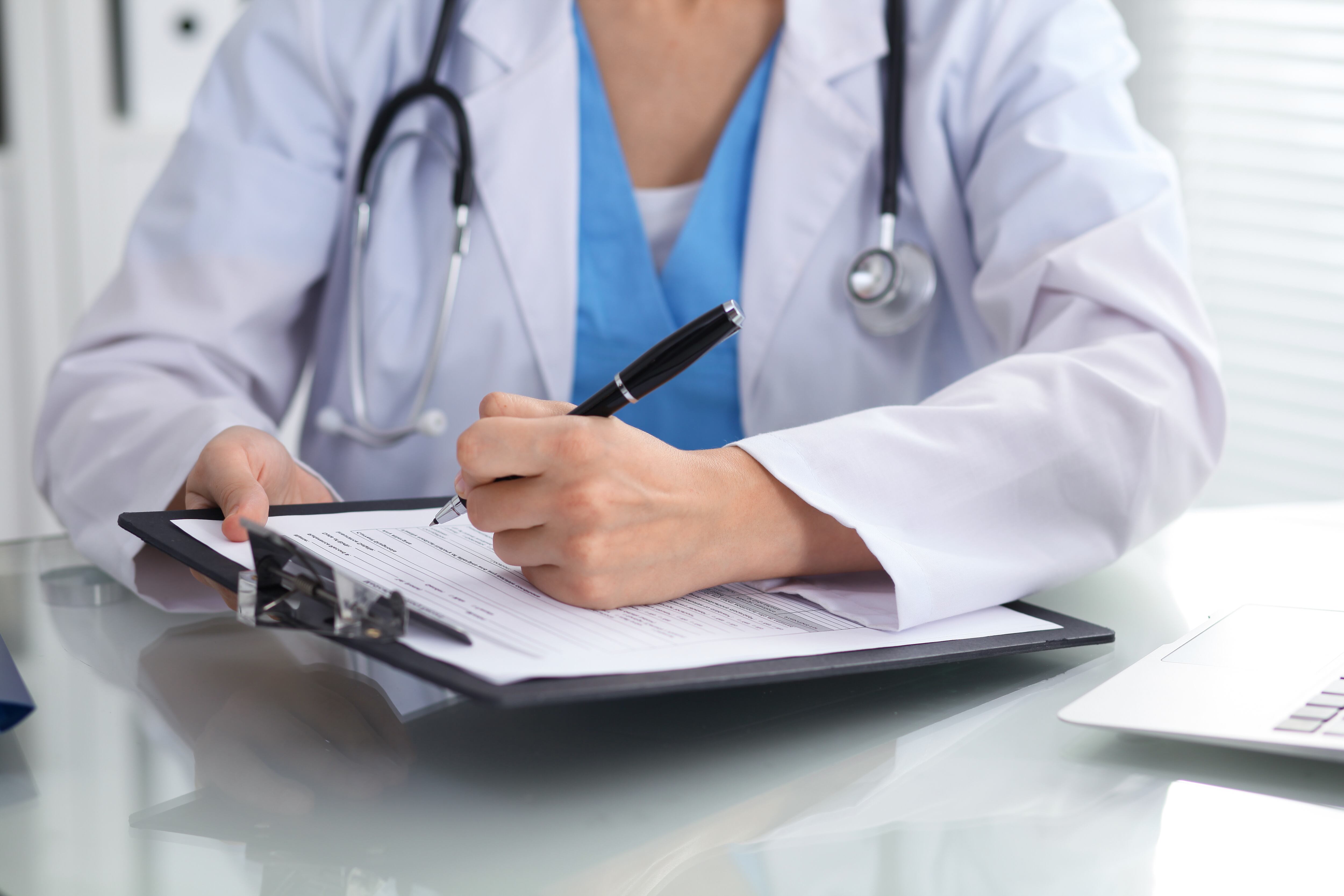 Doctor woman filling up medical form while sitting at the table, close-up of hands.