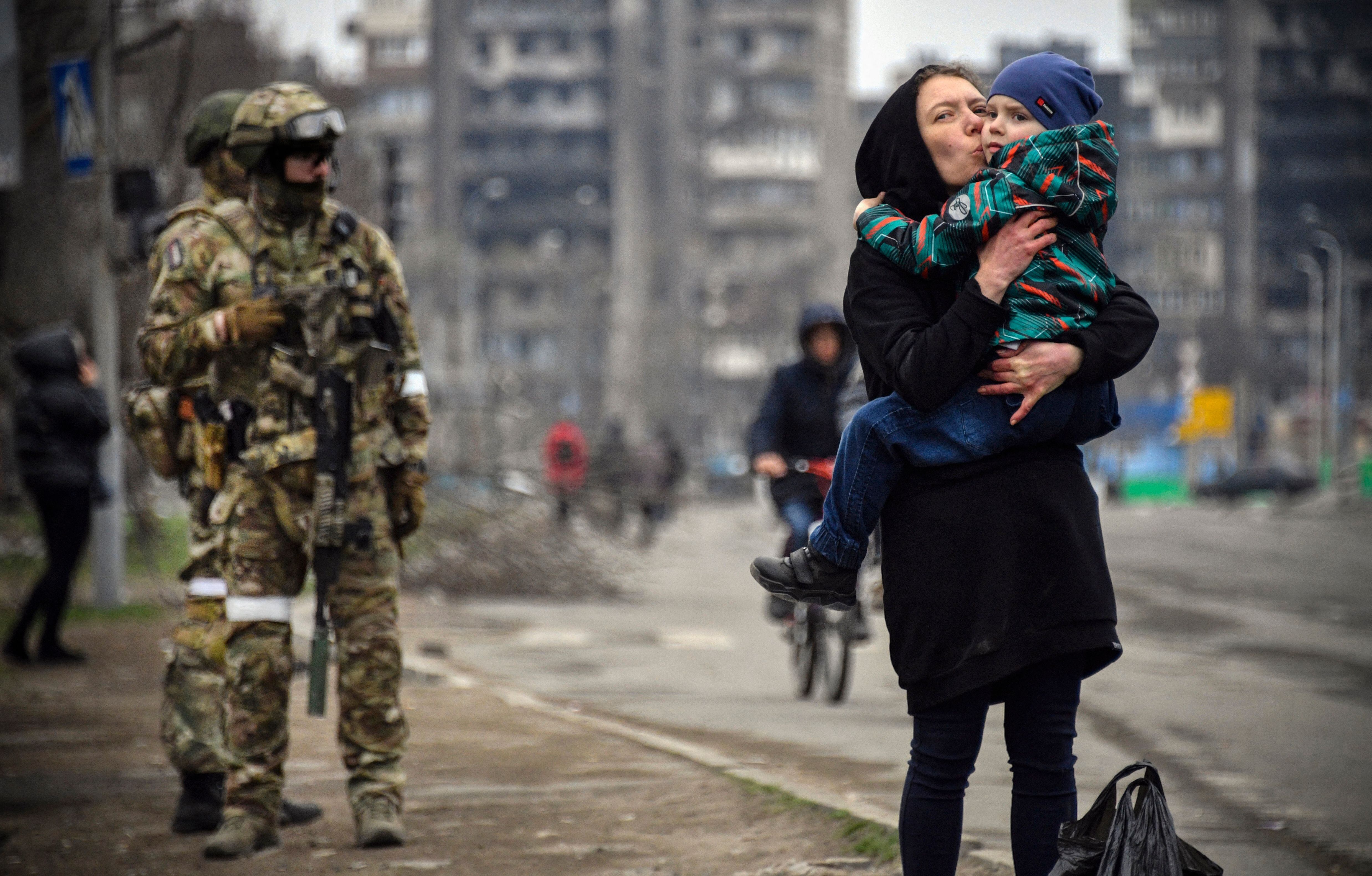 TOPSHOT - A woman holds and kisses a child next to Russian soldiers in a street of Mariupol on April 12, 2022, as Russian troops intensify a campaign to take the strategic port city, part of an anticipated massive onslaught across eastern Ukraine, while Russia's President makes a defiant case for the war on Russia's neighbour. - *EDITOR'S NOTE: This picture was taken during a trip organized by the Russian military.* (Photo by Alexander NEMENOV / AFP) (Photo by ALEXANDER NEMENOV/AFP via Getty Images)