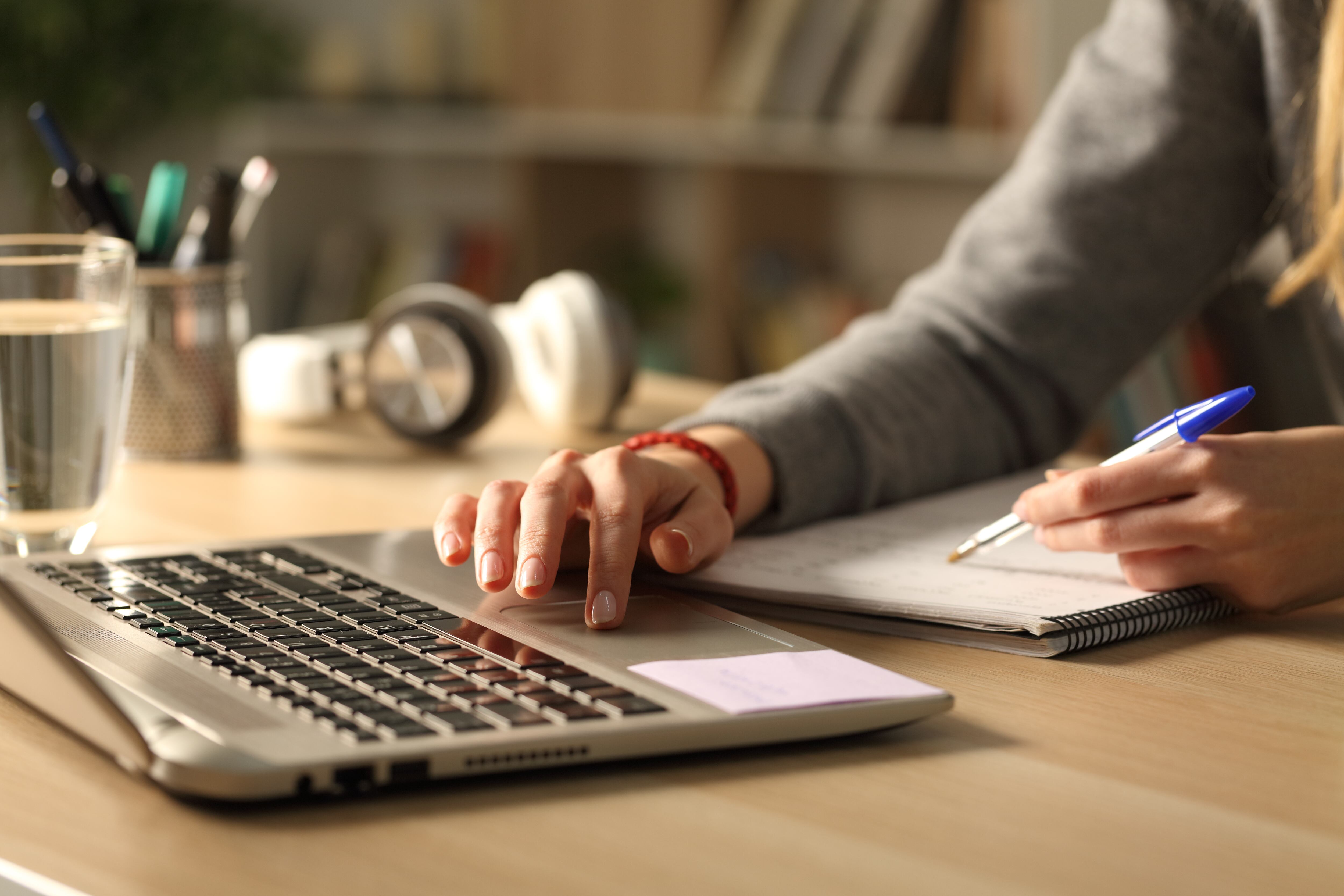Close up of student girl hands comparing notes on laptop sitting on a desk at home at night