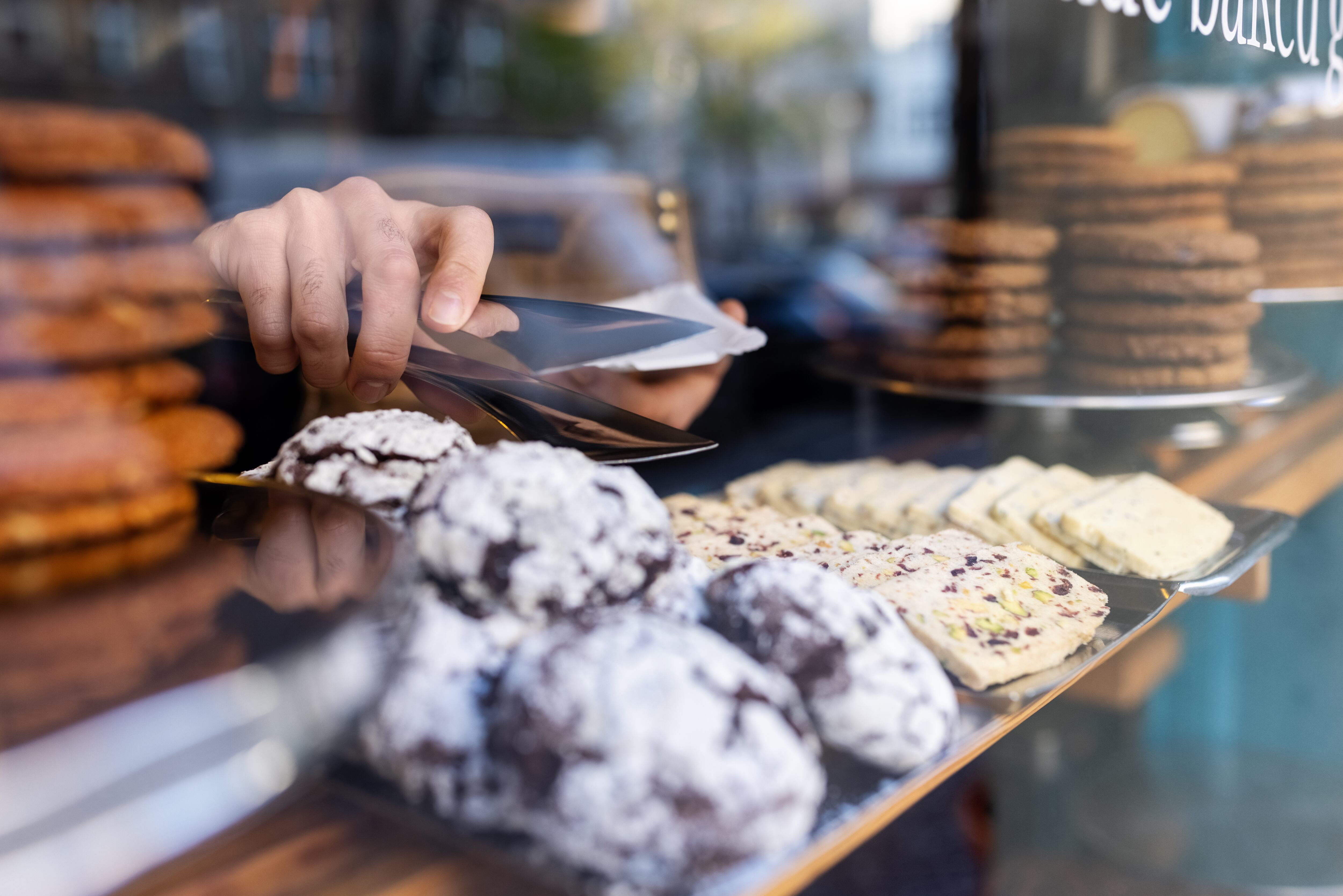 Close-up of freshly baked sweet food in the display cabinet in a cafe. Waiter picking up food from display cabinet for serving at the bakery.