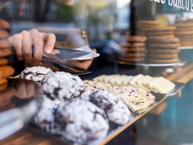 Close-up of freshly baked sweet food in the display cabinet in a cafe. Waiter picking up food from display cabinet for serving at the bakery.