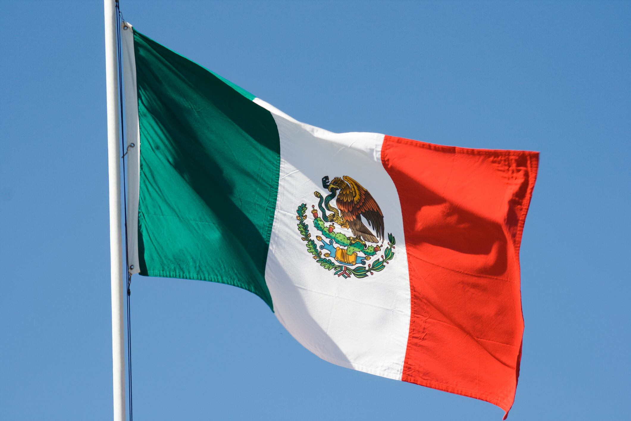 Horizontal view of a Mexican national flag waving in the wind against a clear blue sky.