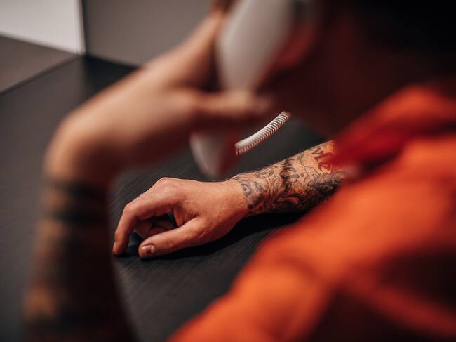 One man, male prisoner sitting in prison visit room, talking on phone.