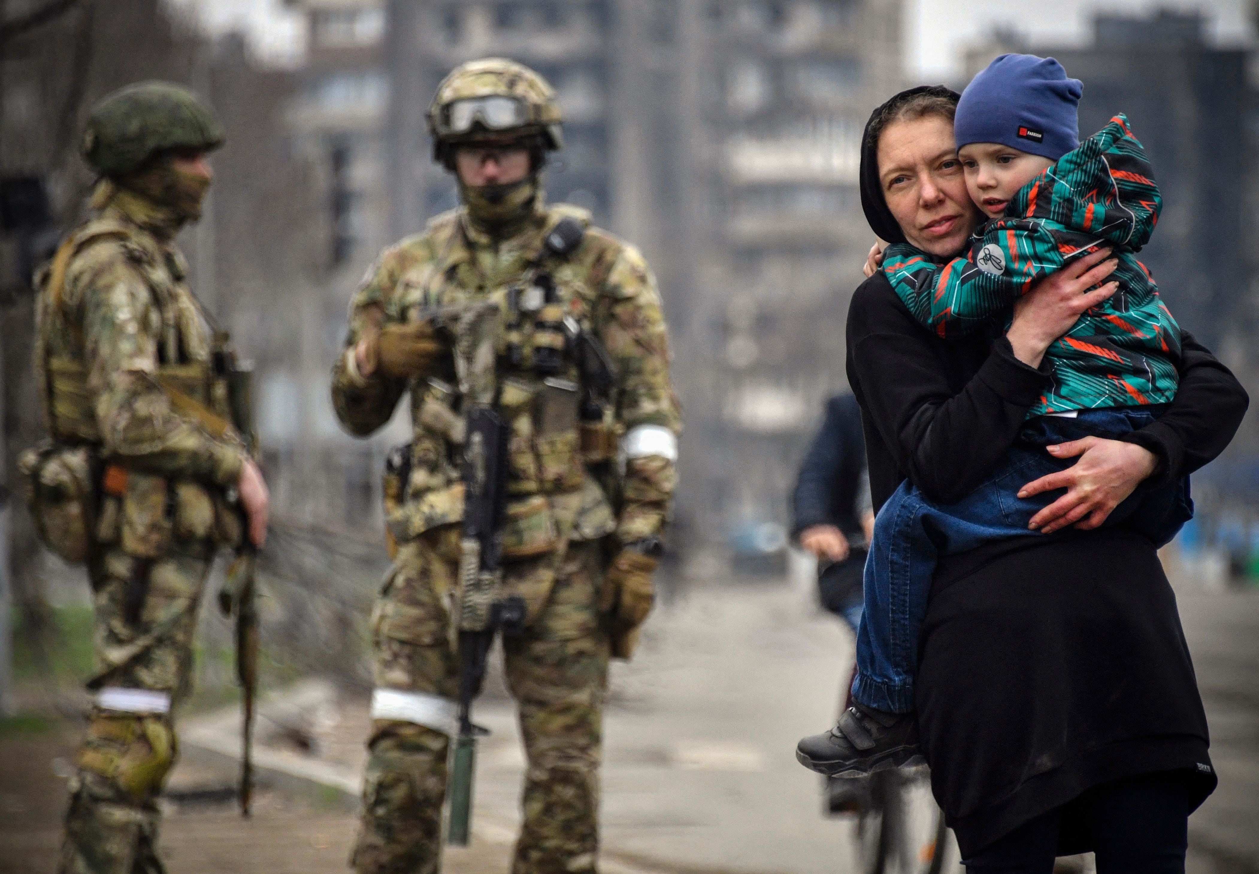 A woman holds a child next to Russian soldiers in a street of Mariupol on April 12, 2022, as Russian troops intensify a campaign to take the strategic port city, part of an anticipated massive onslaught across eastern Ukraine, while Russia's President makes a defiant case for the war on Russia's neighbour. - *EDITOR'S NOTE: This picture was taken during a trip organized by the Russian military.* (Photo by Alexander NEMENOV / AFP) (Photo by ALEXANDER NEMENOV/AFP via Getty Images)