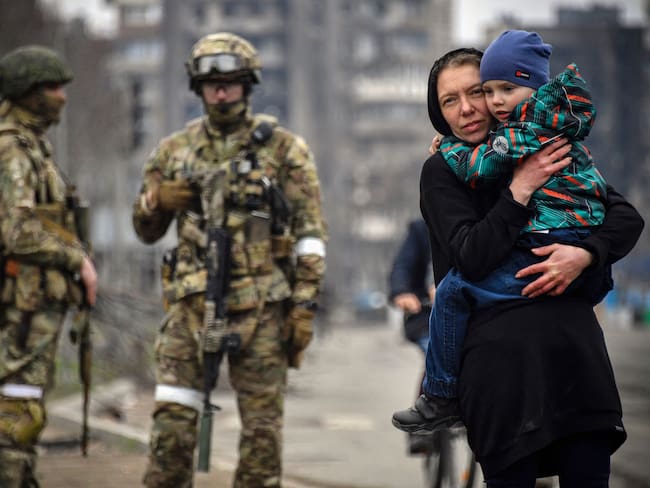 A woman holds a child next to Russian soldiers in a street of Mariupol on April 12, 2022, as Russian troops intensify a campaign to take the strategic port city, part of an anticipated massive onslaught across eastern Ukraine, while Russia&#039;s President makes a defiant case for the war on Russia&#039;s neighbour. - *EDITOR&#039;S NOTE: This picture was taken during a trip organized by the Russian military.* (Photo by Alexander NEMENOV / AFP) (Photo by ALEXANDER NEMENOV/AFP via Getty Images)