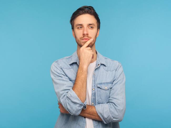Hmm, let's think! Portrait of pensive handsome man in worker denim shirt touching chin while pondering plan, having doubts about difficult choice, not sure. studio shot isolated on blue background
