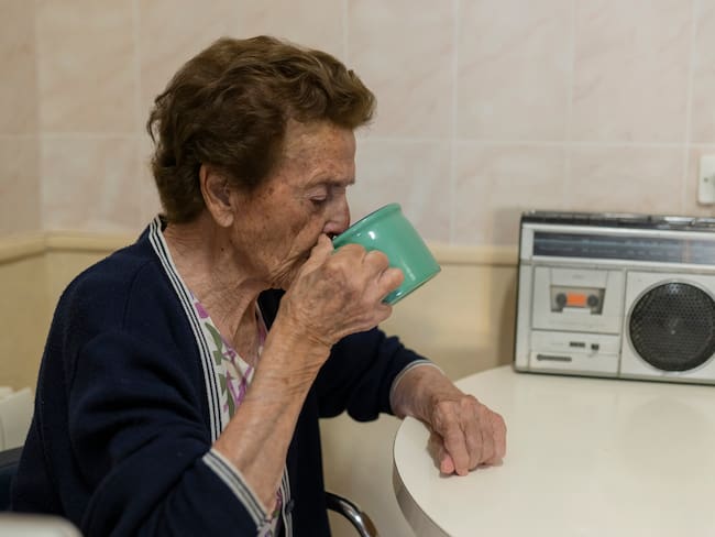 Mujer mayor tomando una bebida caliente mientras escucha radio (Getty Images)