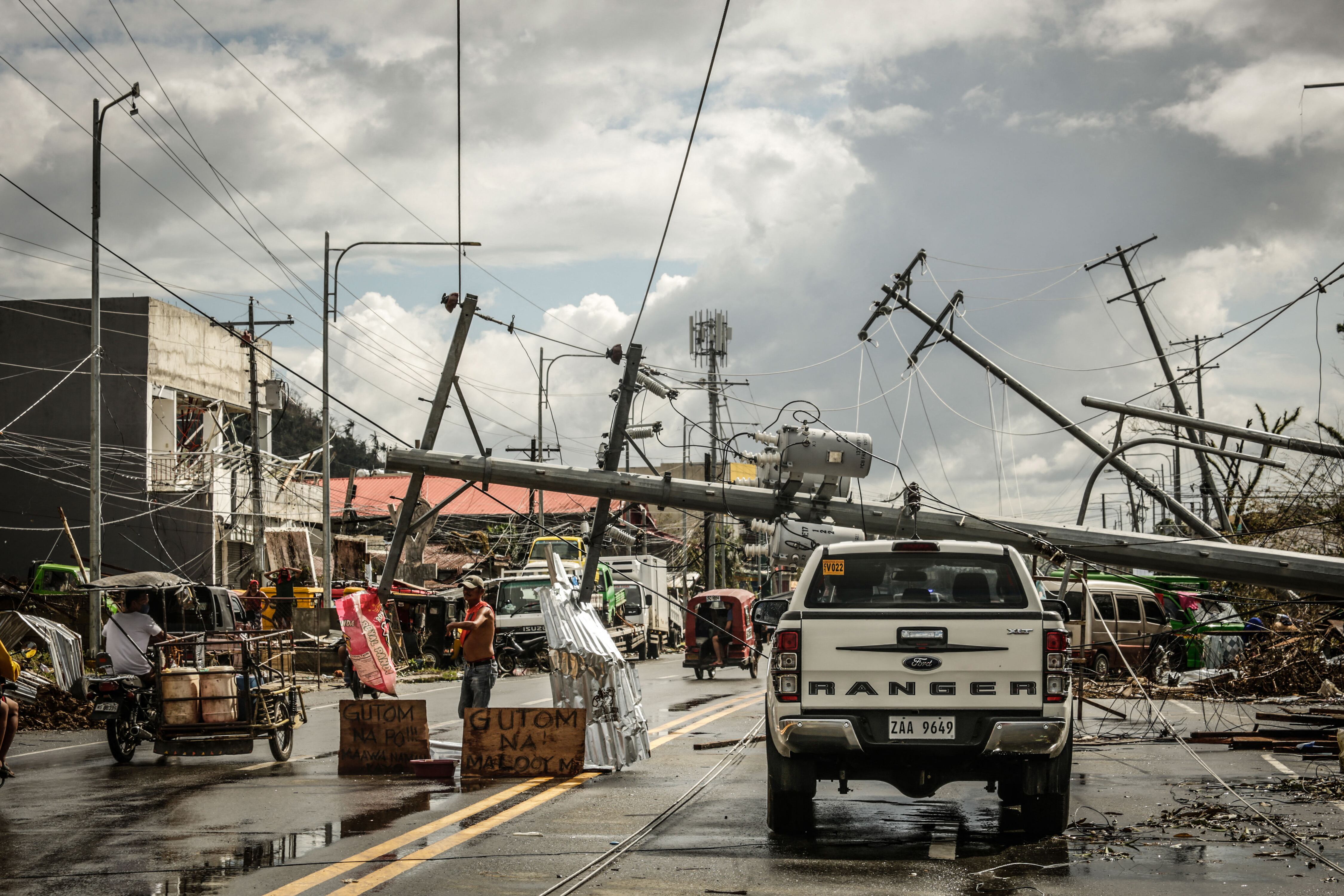 TOPSHOT - Fallen electric pylons block a road while a sign asking for food (L) is displayed along a road in Surigao City, Surigao del norte province, on December 19, 2021, days after super Typhoon Rai devastated the city. (Photo by Ferdinandh CABRERA / AFP) (Photo by FERDINANDH CABRERA/AFP via Getty Images)