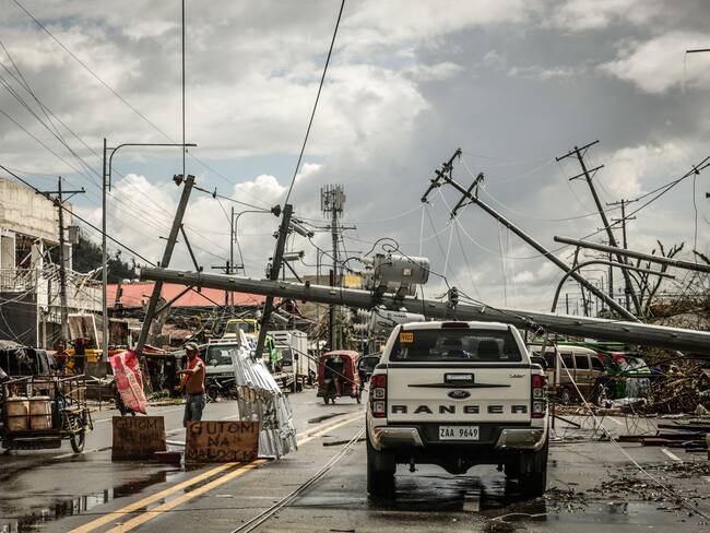 TOPSHOT - Fallen electric pylons block a road while a sign asking for food (L) is displayed along a road in Surigao City, Surigao del norte province, on December 19, 2021, days after super Typhoon Rai devastated the city. (Photo by Ferdinandh CABRERA / AFP) (Photo by FERDINANDH CABRERA/AFP via Getty Images)
