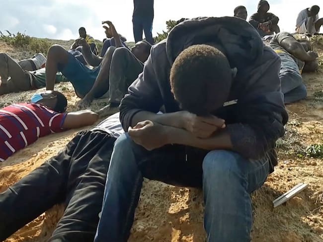 A video grab shows migrant survivors of a deadly shipwreck siting on a sandy beach on the coast of al-Khums, a port city 120 kilometres (75 miles) west of the Libyan capital Tripoli, on November 12, 2020. - According to the United Nations 74 people died in the deadly shipwreck off the Libyan coast, the latest in a spate of migrant vessel sinkings in the central Mediterranean. This year has seen a resurgence of boats in the central Mediterranean, a well-trodden but often deadly route for those hoping to travel to Europe, mainly embarking from Libya and neighbouring Tunisia. (Photo by - / various sources / AFP) (Photo by -/AFP via Getty Images)