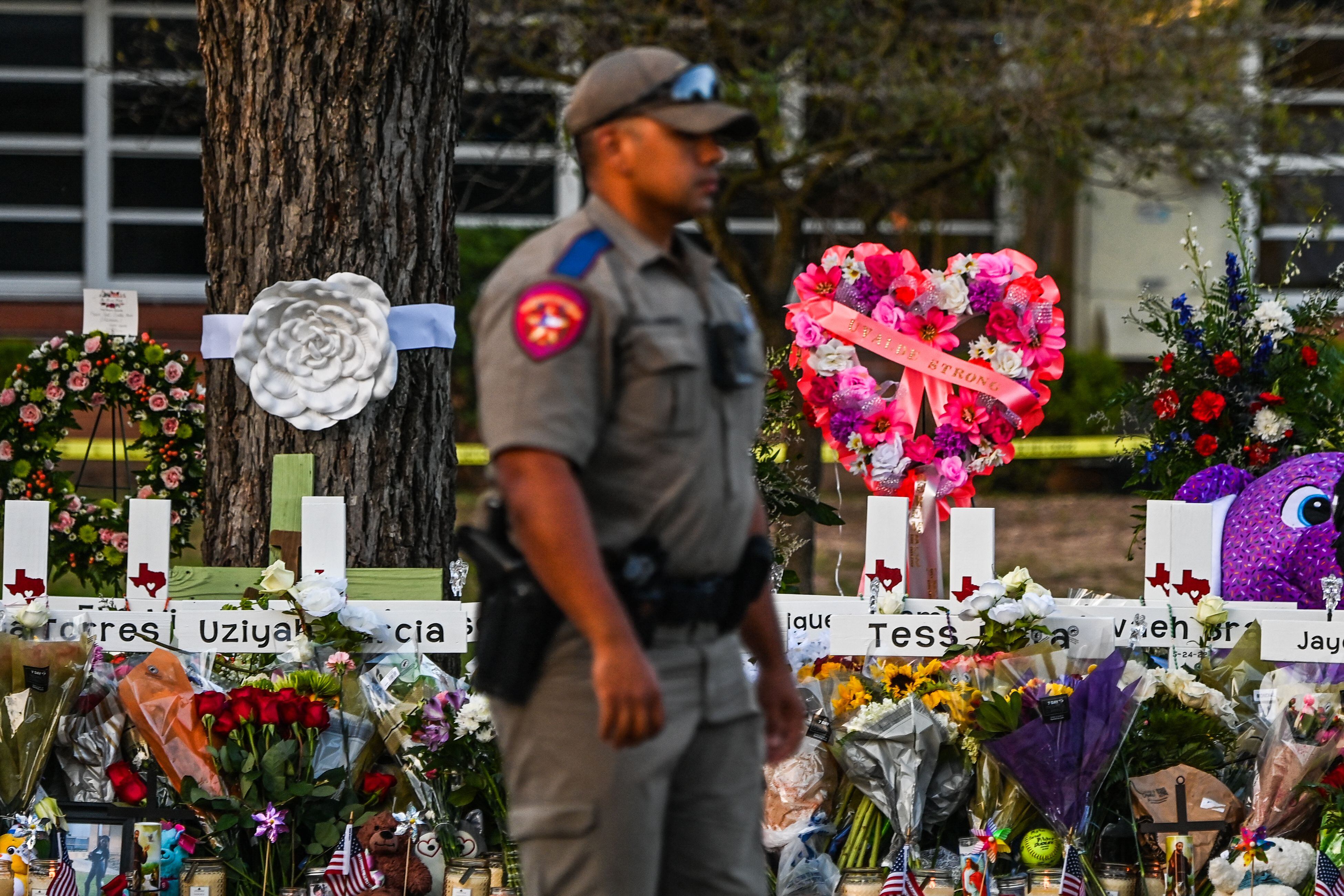 A police officer stands near a makeshift memorial for the shooting victims outside Robb Elementary School in Uvalde, Texas, on May 27, 2022. - Texas police faced angry questions May 26, 2022 over why it took an hour to neutralize the gunman who murdered 19 small children and two teachers in Uvalde, as video emerged of desperate parents begging officers to storm the school. (Photo by CHANDAN KHANNA / AFP) (Photo by CHANDAN KHANNA/AFP via Getty Images)