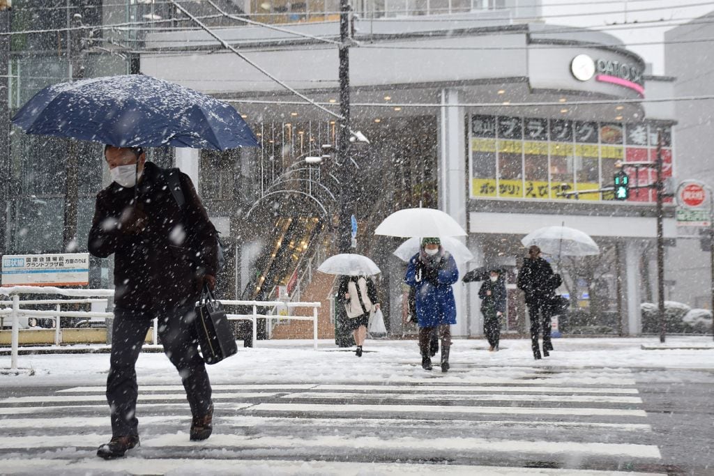 People cross the street as it snows in the city of Toyama, Toyama prefecture on the central-western coast of Japan, on January 24, 2023, as parts of the country brace for a severe winter storm. - Japan OUT (Photo by JIJI Press / AFP) / Japan OUT (Photo by STR/JIJI Press/AFP via Getty Images)
