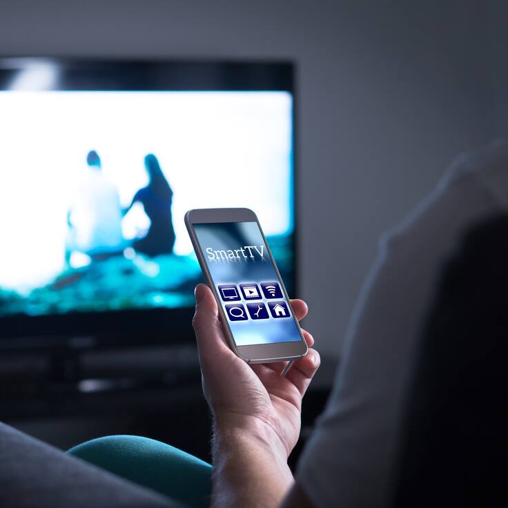 Hombre usando su celular para compartir pantalla al televisor y proyectar una película (GettyImages)