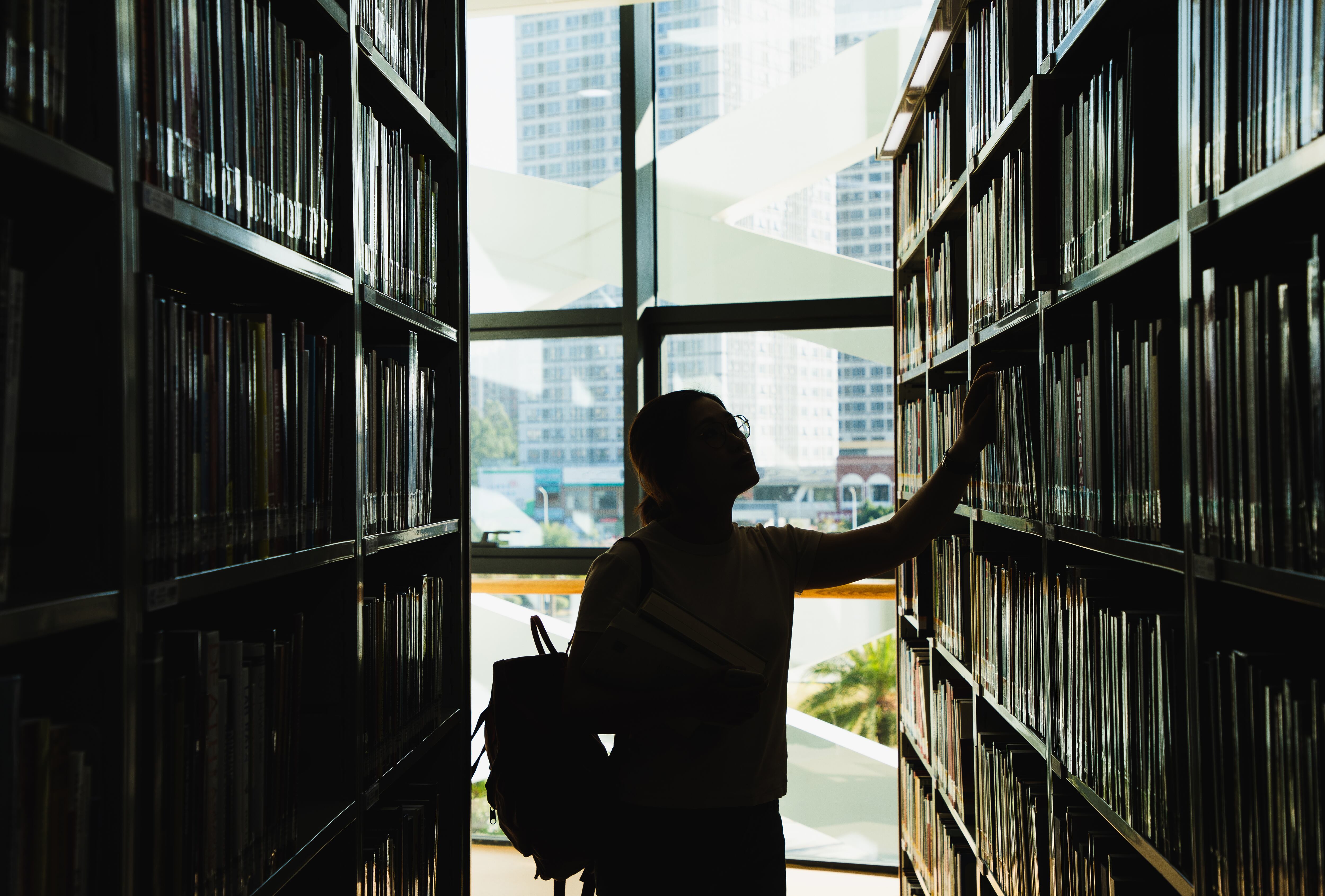 female student in silhouette looking at the books from the bookshelf