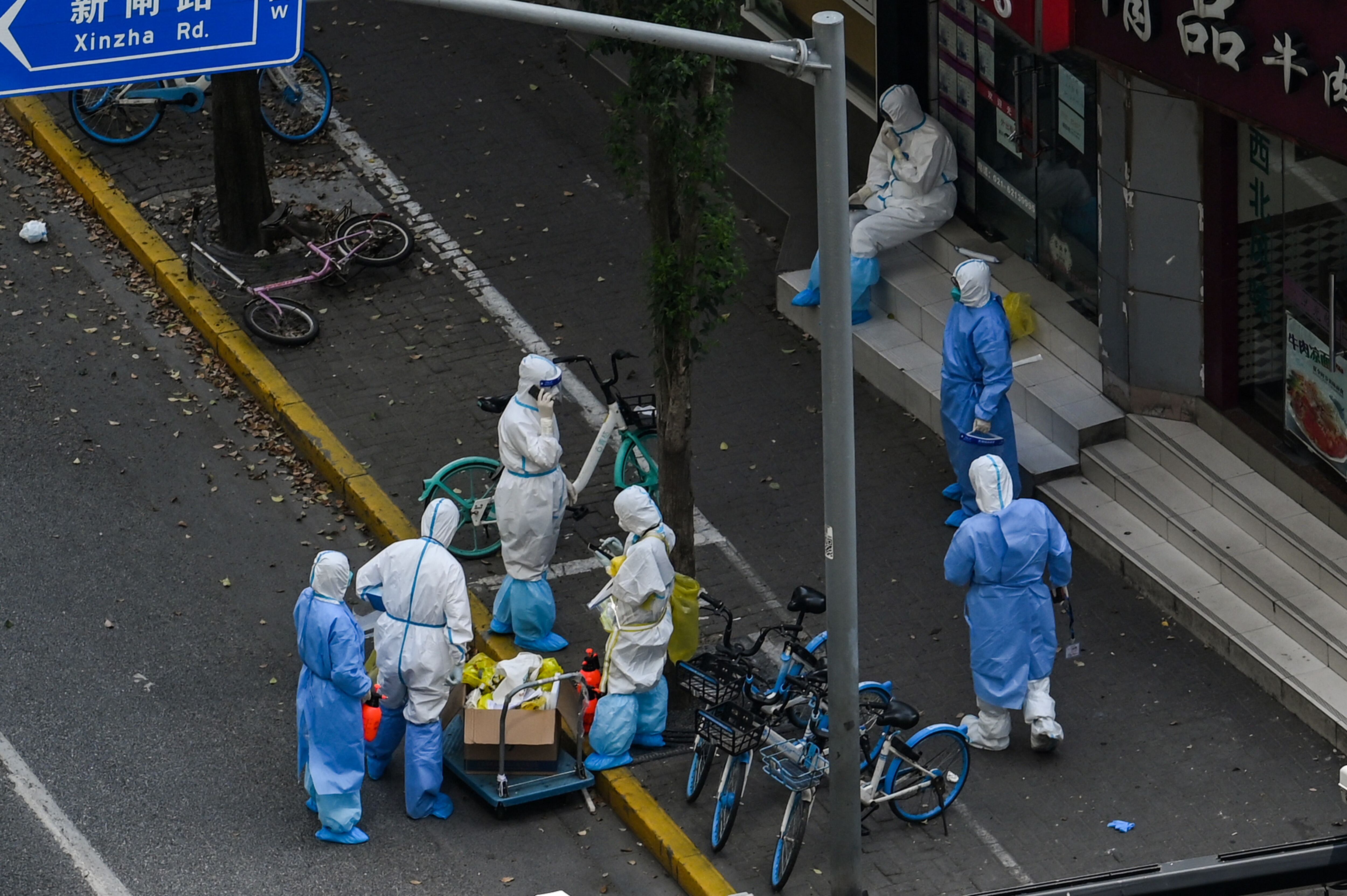 Health workers wearing personal protective equipment (PPE) stand next to the entrance of a neighborhood during a COVID-19 lockdown in the Jing'an district in Shanghai on April 12, 2022. (Photo by HECTOR RETAMAL / AFP) (Photo by HECTOR RETAMAL/AFP via Getty Images)