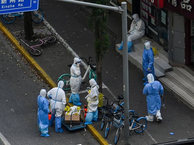 Health workers wearing personal protective equipment (PPE) stand next to the entrance of a neighborhood during a COVID-19 lockdown in the Jing'an district in Shanghai on April 12, 2022. (Photo by HECTOR RETAMAL / AFP) (Photo by HECTOR RETAMAL/AFP via Getty Images)