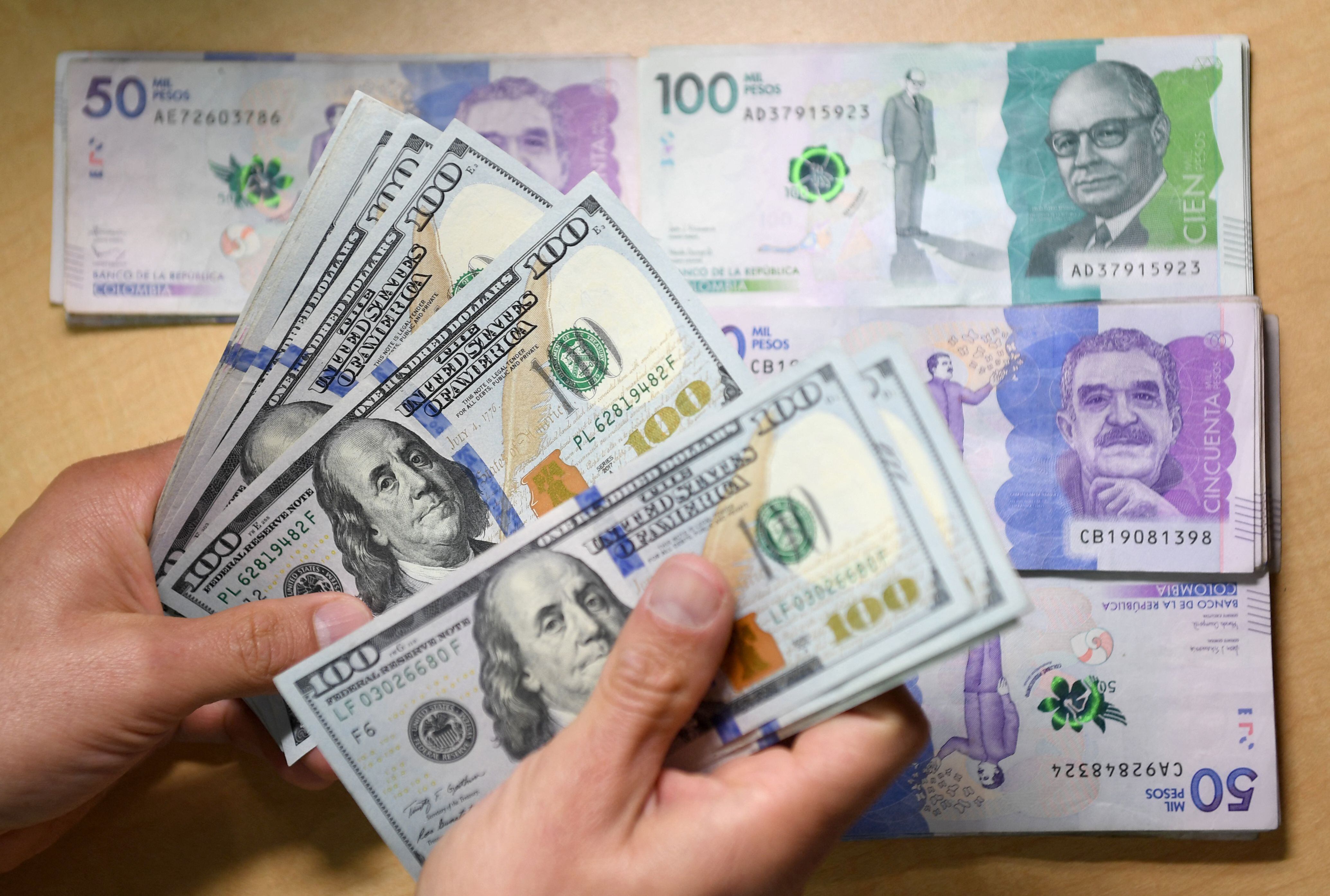 Un hombre cuenta billetes de cien dólares estadounidenses mientras los billetes en pesos colombianos permanecen sobre una mesa en Bogotá, el 24 de octubre de 2022. (Daniel Muñoz/AFP vía Getty Images)