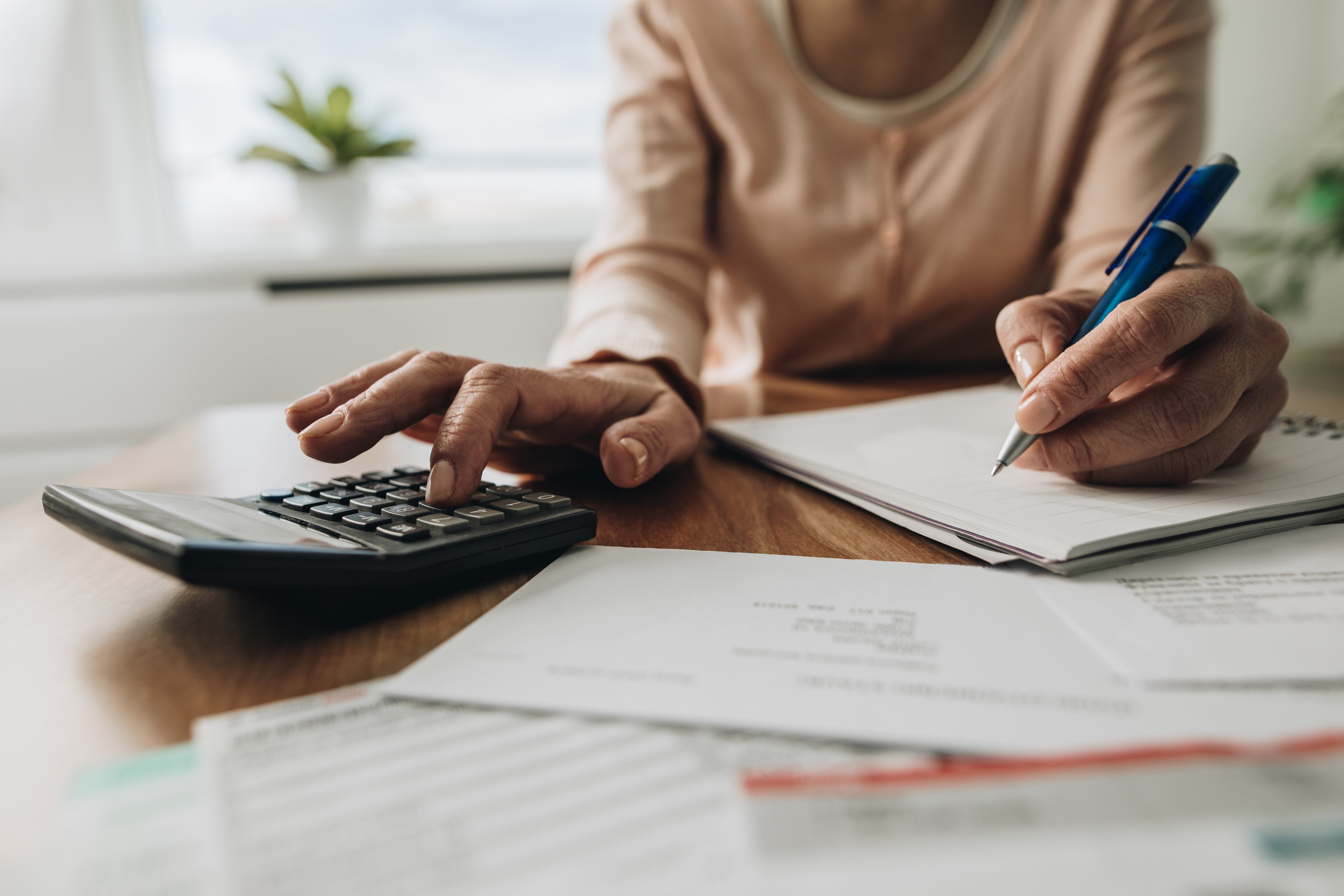 Close up of unrecognizable woman using calculator while going through bills and home finances.