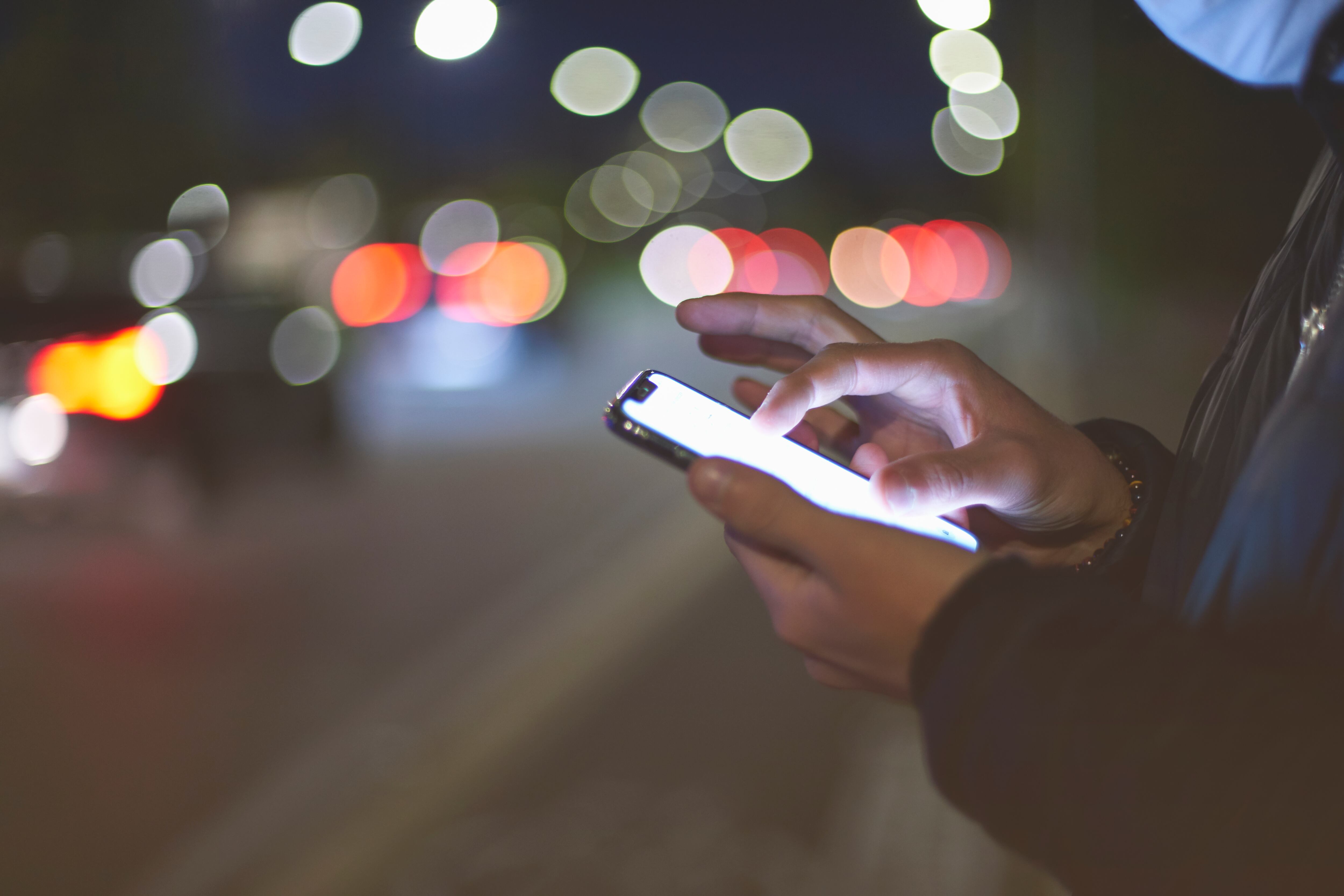 Close-up of man using smart phone. Defocused traffic lights on background