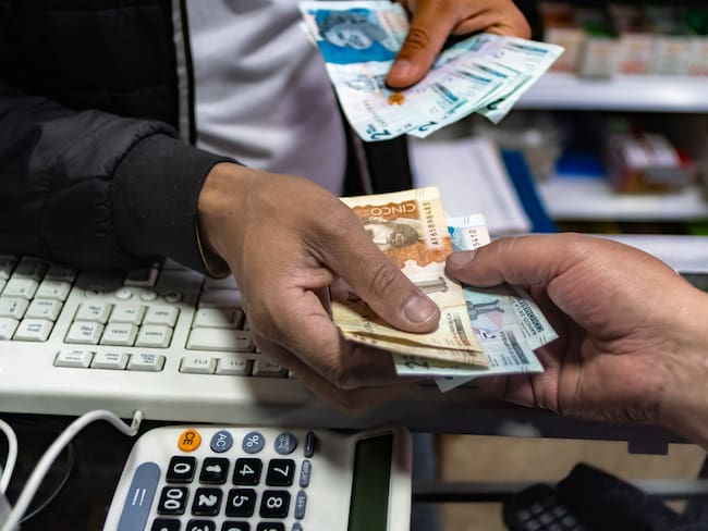 Manos de un hombre con monedas y billetes de Colombia. Getty Images