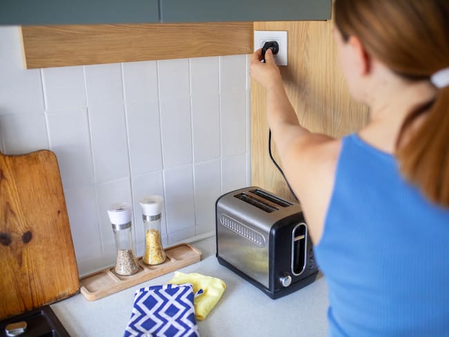 Mujer desenchufando una tostadora luego de hacer el desayuno en su hogar (Foto vía GettyImages)