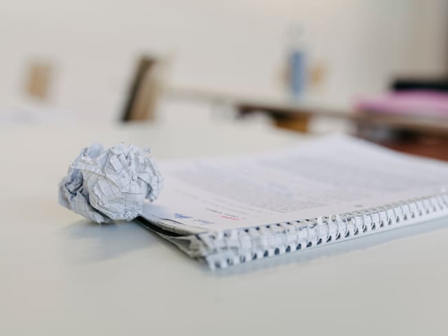 A close up of a scrunched up ball of paper and a students notepad sitting on a high school desk.