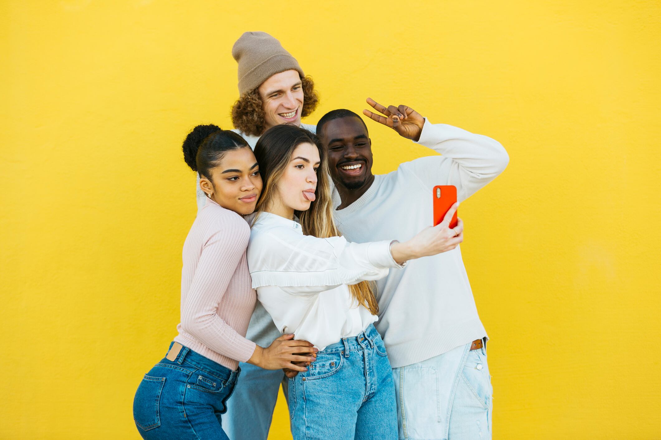 A multi-ethnic group of young boys and girls taking a selfie and posing together in front of a yellow background