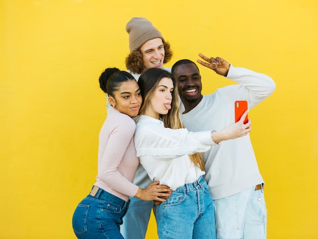 A multi-ethnic group of young boys and girls taking a selfie and posing together in front of a yellow background