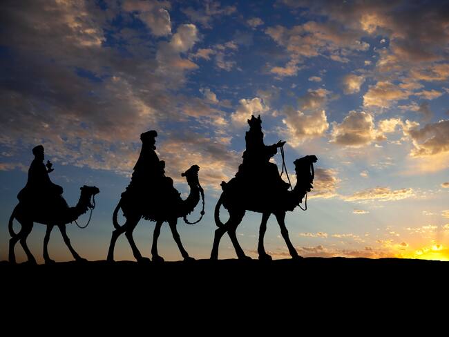 Los tres reyes en camellos contra un sol poniente.