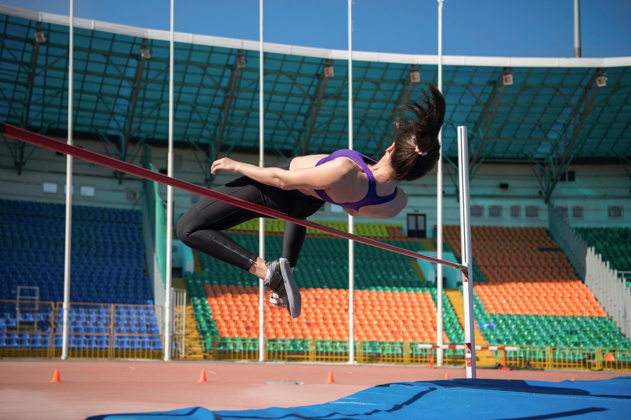 Strong female athlete jumping over bar during track and field workout on stadium