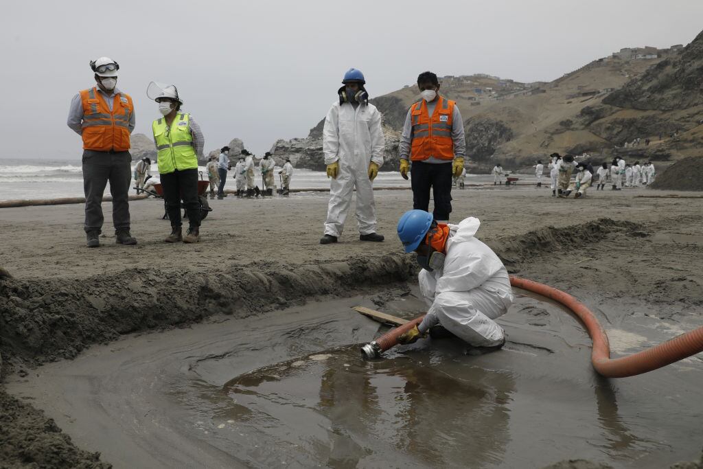 LIMA, PERU - JANUARY 20: Cleaning teams work to remove oil at the shores after an oil spill in the Ventanilla Sea in the province of Callao has stained the beaches of the district area in Lima, Peru on January 20, 2022. The spill was recorded on Saturday, January 15, during the unloading of crude oil from a ship at the La Pampilla Refinery, after strong waves reached the Peruvian coast as a result of the underwater volcanic eruption near Tonga. On January 20, the district of Ventanilla asks the government to declare an environmental emergency after the oil spill, in addition to groups of people and animalists who came to the rescue of various types of birds. (Photo by Klebher Vasquez/Anadolu Agency via Getty Images)