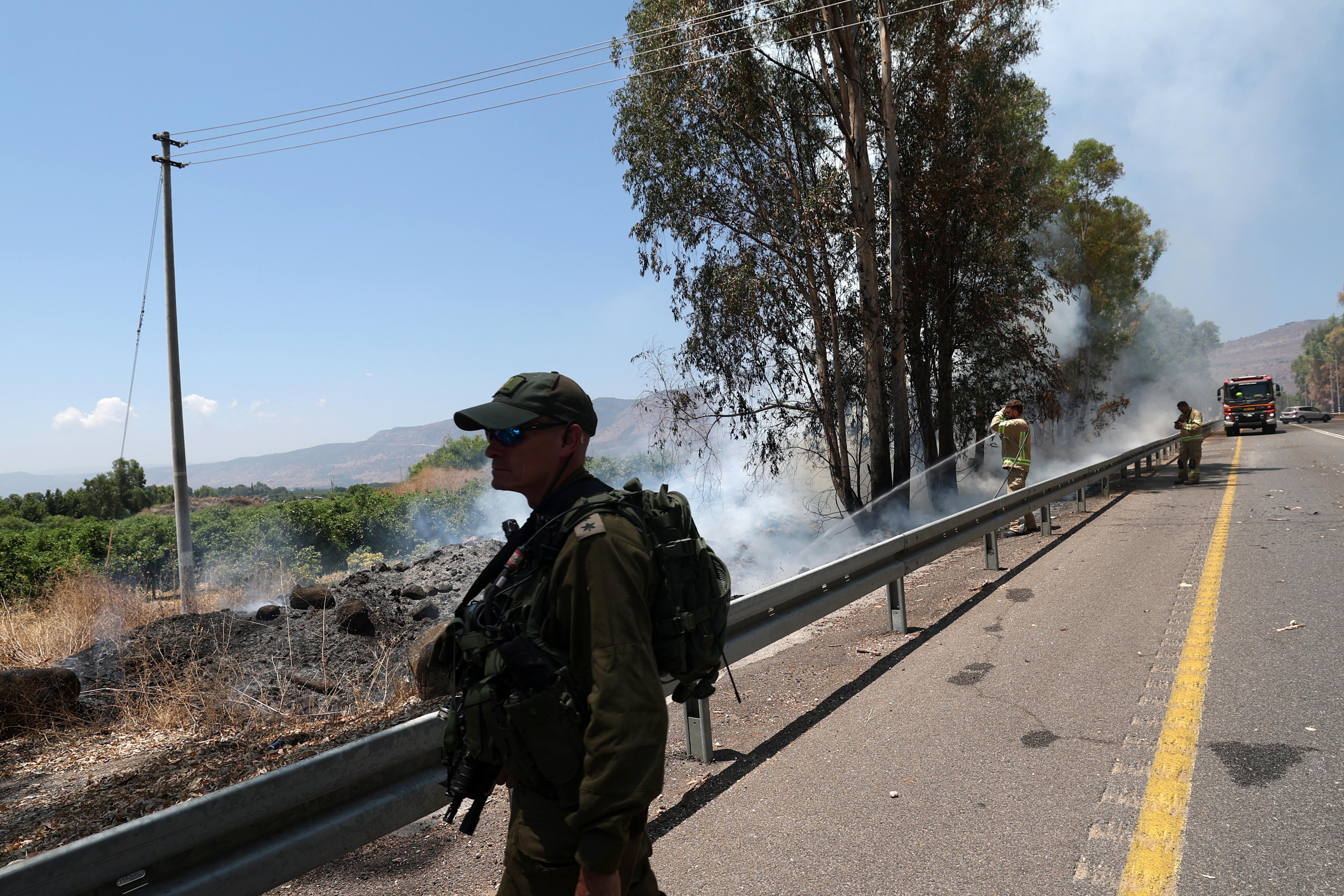 Beit Hillel (Israel), 17/07/2024.- An armed officer keeps watch as firefighters try to extinguish a fire caused by projectiles fired from southern Lebanon, along a road near Beit Hillel, northern Israel, 17 July 2024. The Israeli military stated on 17 July, that approximately 15 projectiles were identified crossing from Lebanon in the area of Nahariyya. (Líbano) EFE/EPA/ATEF SAFADI