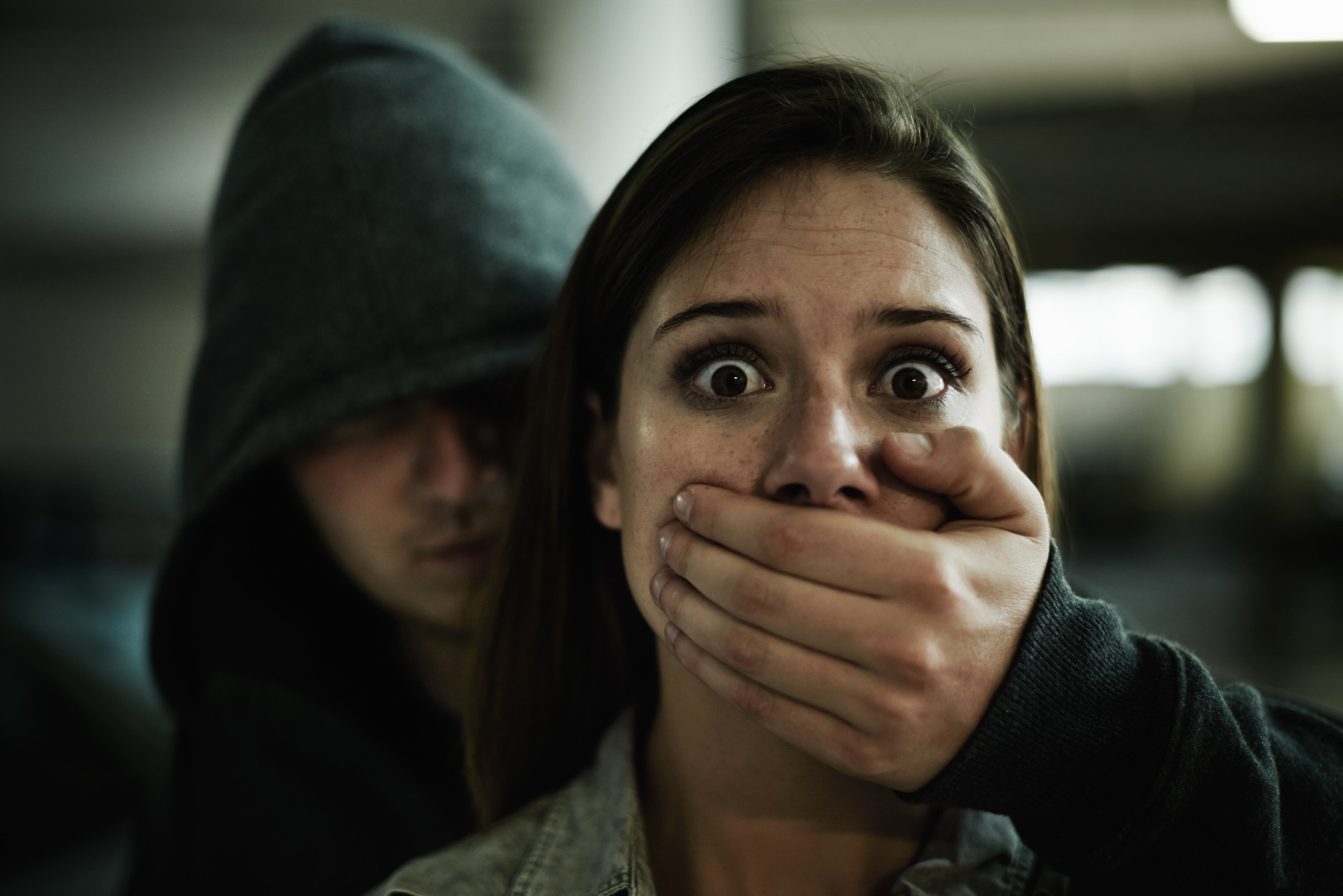 A terrified young woman held captive by a man with his hand over her mouth