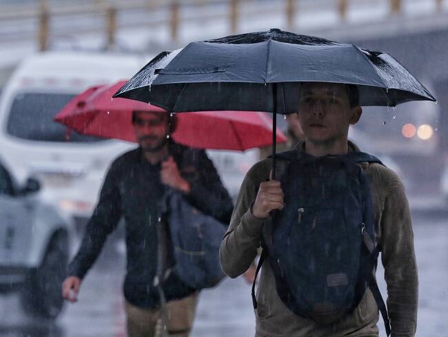 Personas caminando con sombrilla por Bogotá mientras llueve. (Foto vía COLPRENSA)
