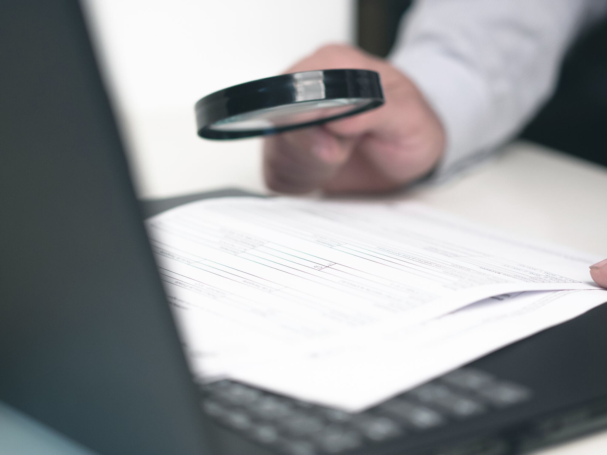 Businessman reading online documents on laptop screen with magnifying glass concept for analyzing a finance agreement or legal contract