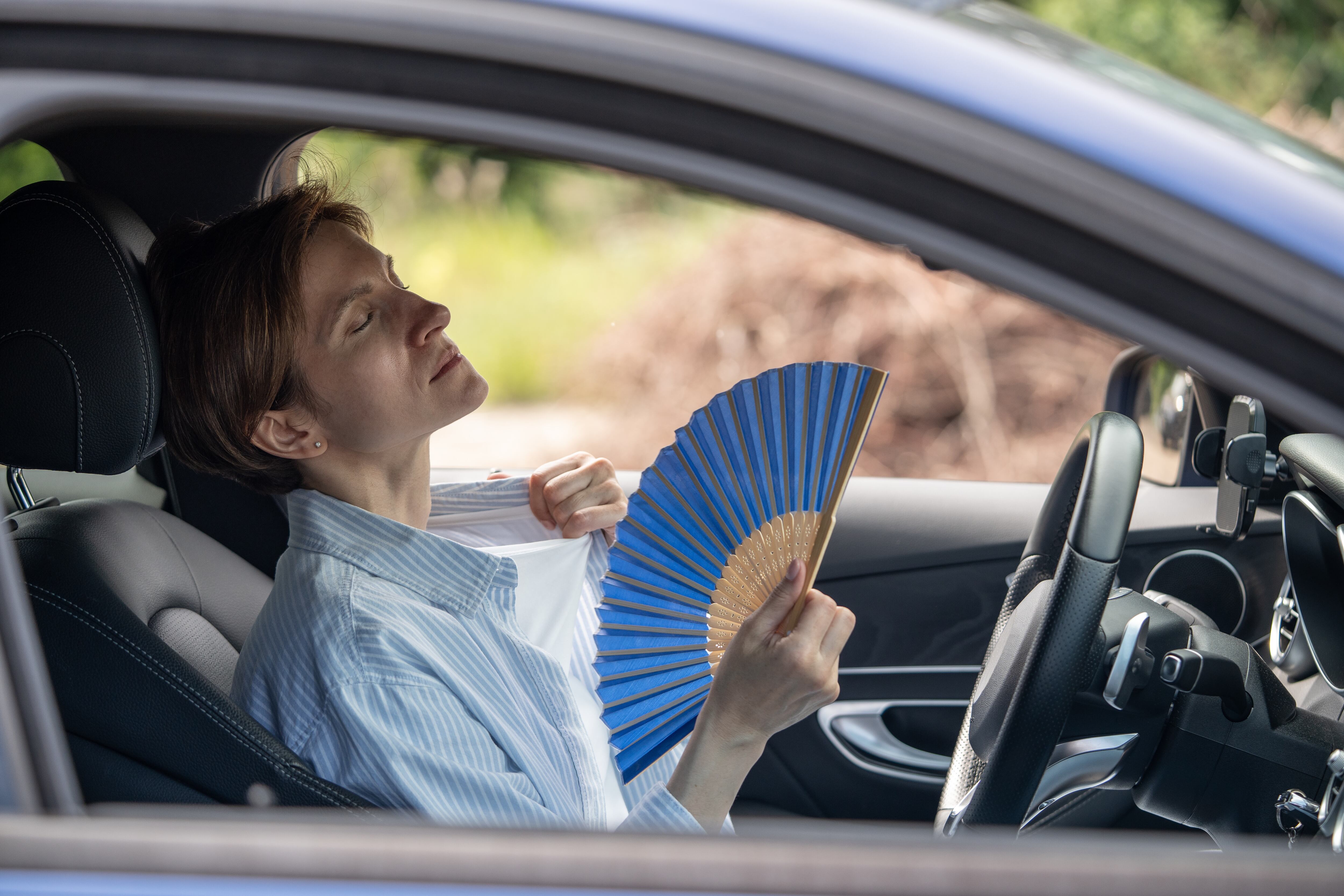 Mujer con calor usando un abanico dentro del carro porque no le funciona el aire acondicionado (Foto vía GettyImages)