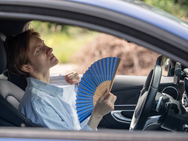 Mujer con calor usando un abanico dentro del carro porque no le funciona el aire acondicionado (Foto vía GettyImages)